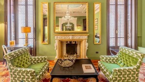 A room with a fireplace, two green patterned armchairs, a black coffee table, and a chandelier. - PALAZZO TREZZA VERONA Preferred Hotels & Resorts (Verona)