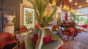 A lobby with a large palm tree, red and grey chairs, hanging lanterns, and a glass display case. - PALAZZO TREZZA VERONA Preferred Hotels & Resorts (Verona)
