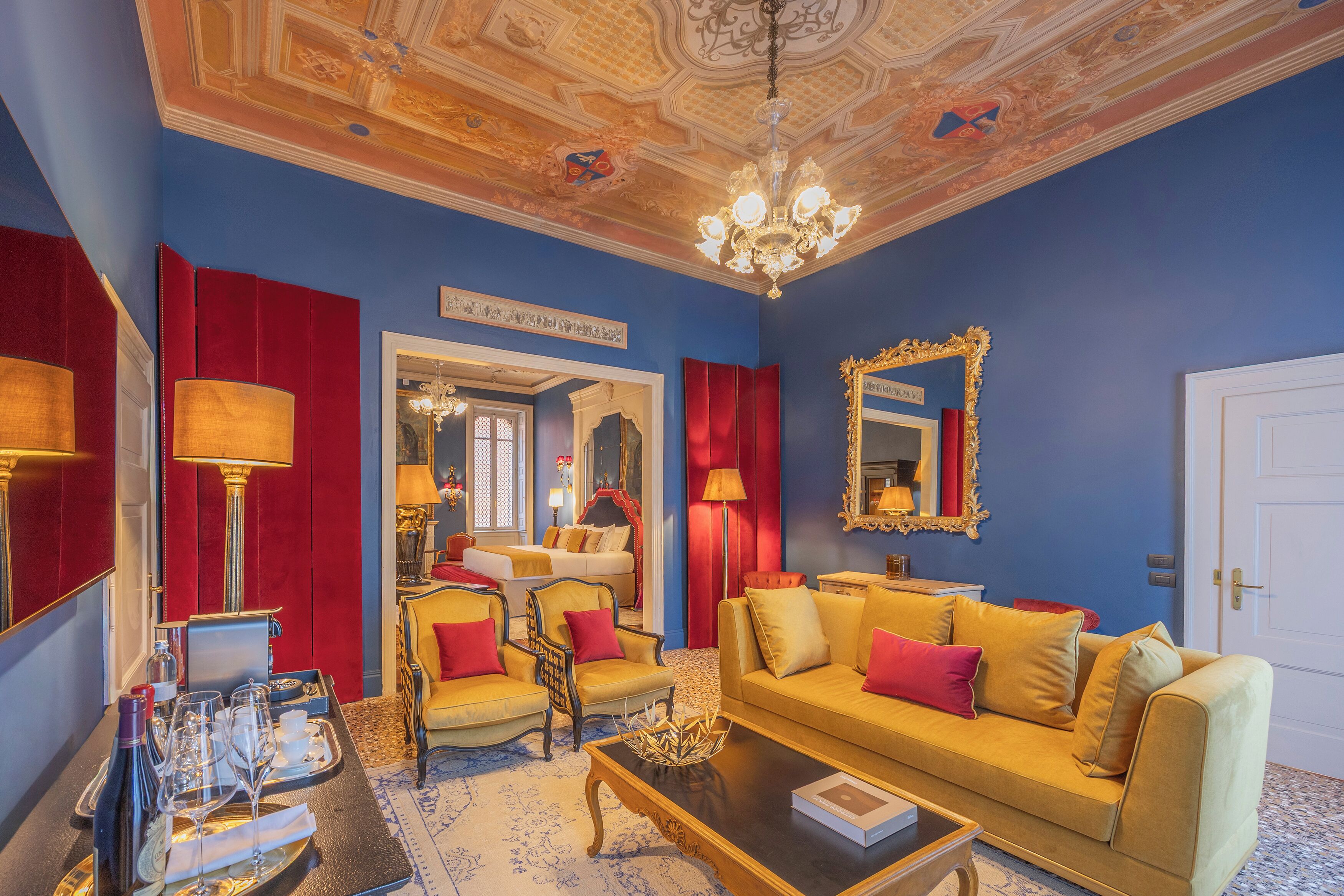 A room with a blue wall, a chandelier, a bed, a sofa, and a mirror.