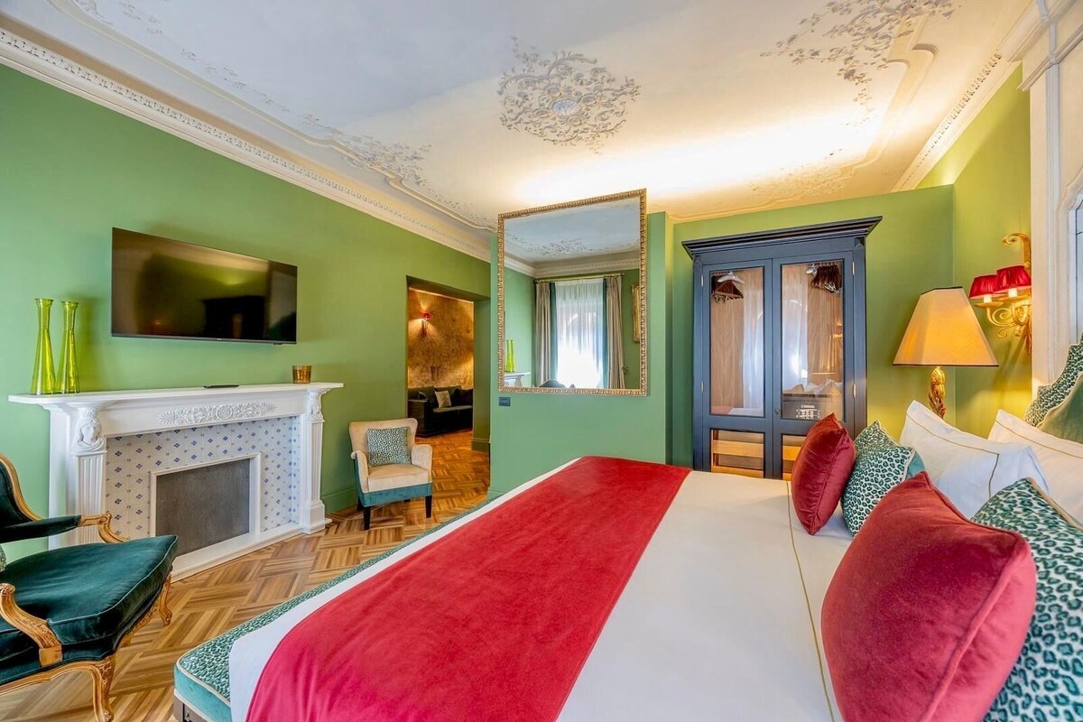 A hotel room with a large bed, a fireplace, a television, and a mirror.