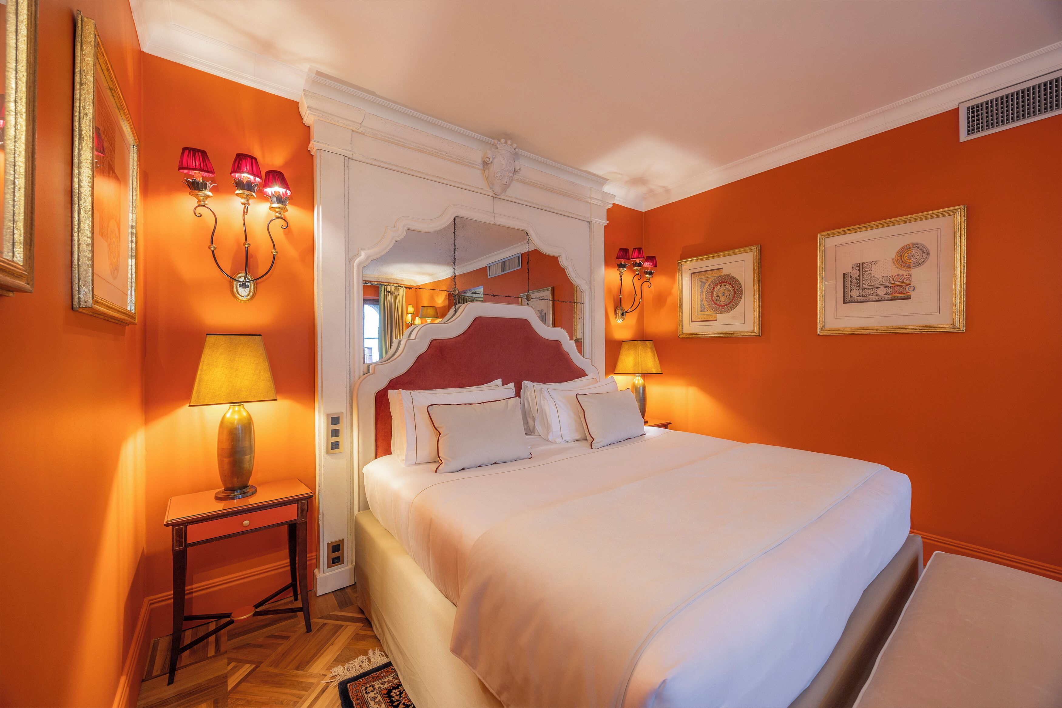Een hotelkamer met een groot bed, twee bedlampjes, een nachtkastje en een spiegel.