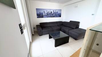 Ein modernes Wohnzimmer mit einem Ecksofa, einem Glastisch und einem Stadtbild an der Wand.