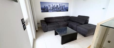 A modern living room with a sectional sofa, a glass coffee table, and a cityscape painting on the wall.