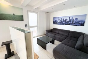 Una sala moderna con un sofá gris, una mesa de centro de vidrio y una pintura de un paisaje urbano.