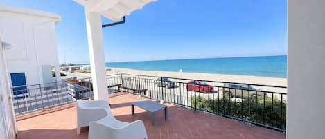 Une terrasse avec vue sur la mer, des chaises blanches, une table et une rambarde.