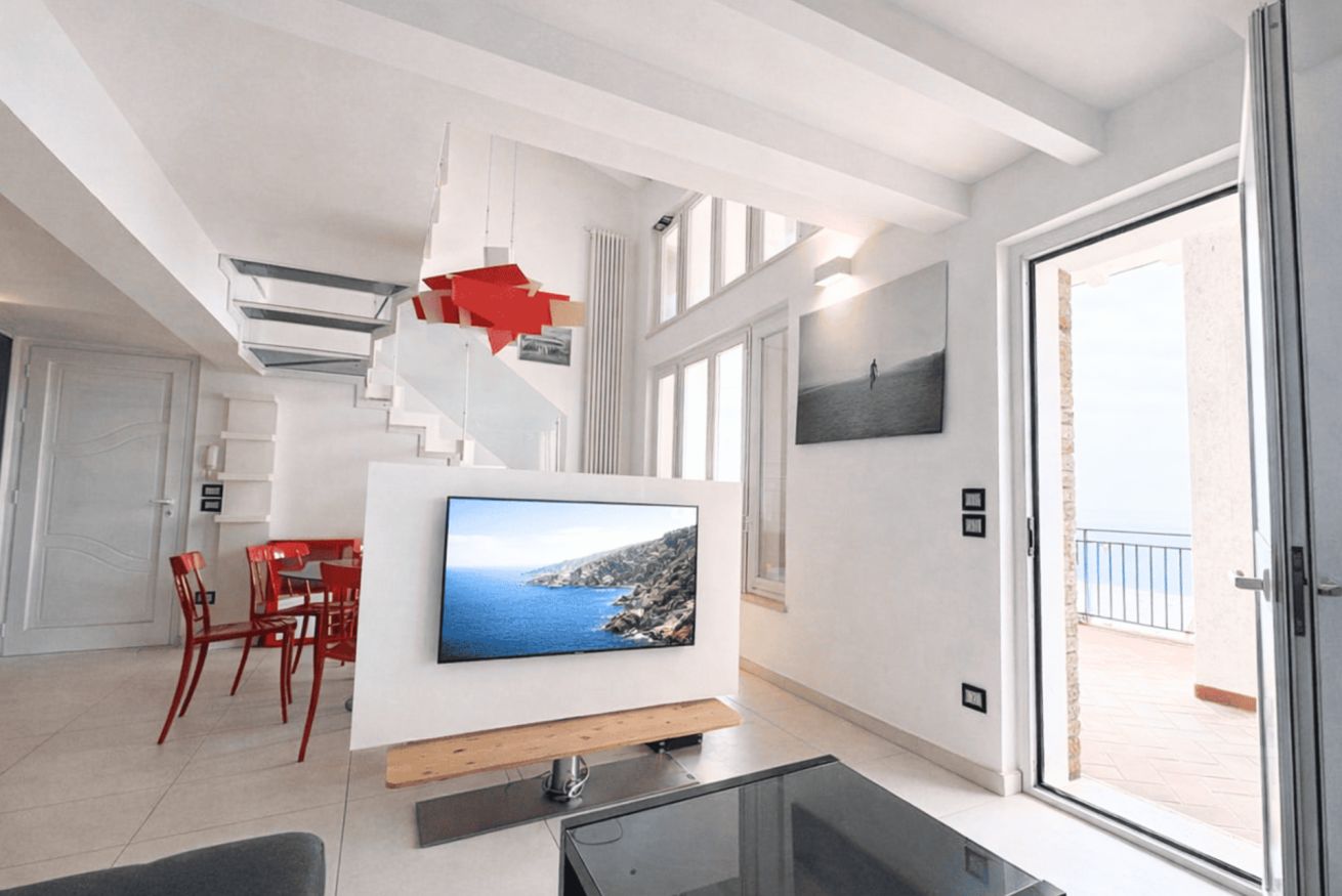 Un salon moderne avec un téléviseur à écran plat, des fauteuils rouges, un escalier et un balcon.