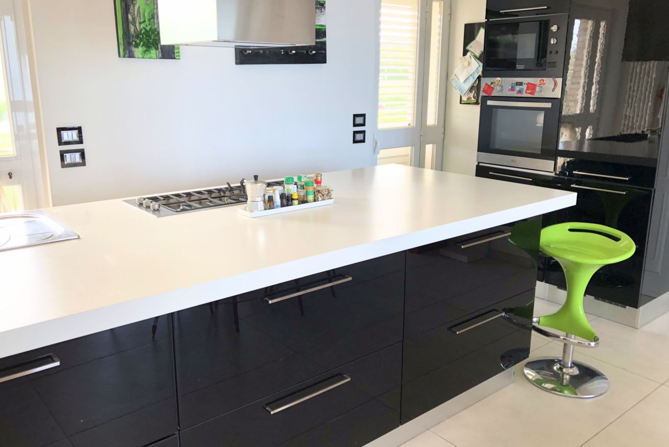 Une cuisine moderne avec un plan de travail blanc, des armoires noires, une hotte en acier inoxydable et un tabouret de bar vert.