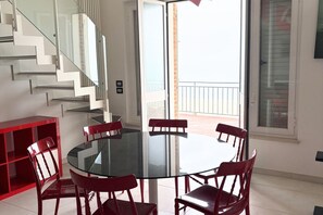 Un interior moderno con una mesa de vidrio rodeada de sillas, una escalera con barandas de vidrio y un balcón con barandilla.
