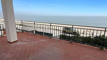 Un balcone con vista sulla spiaggia e sull'oceano, un pavimento in pietra e una ringhiera in metallo nero.