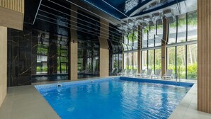 Une piscine intérieure avec des parois en verre transparent, un sol carrelé et une vue sur la verdure environnante.