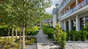 Un chemin menant à un bâtiment moderne doté de nombreux balcons, entouré de verdure et d’arbres.