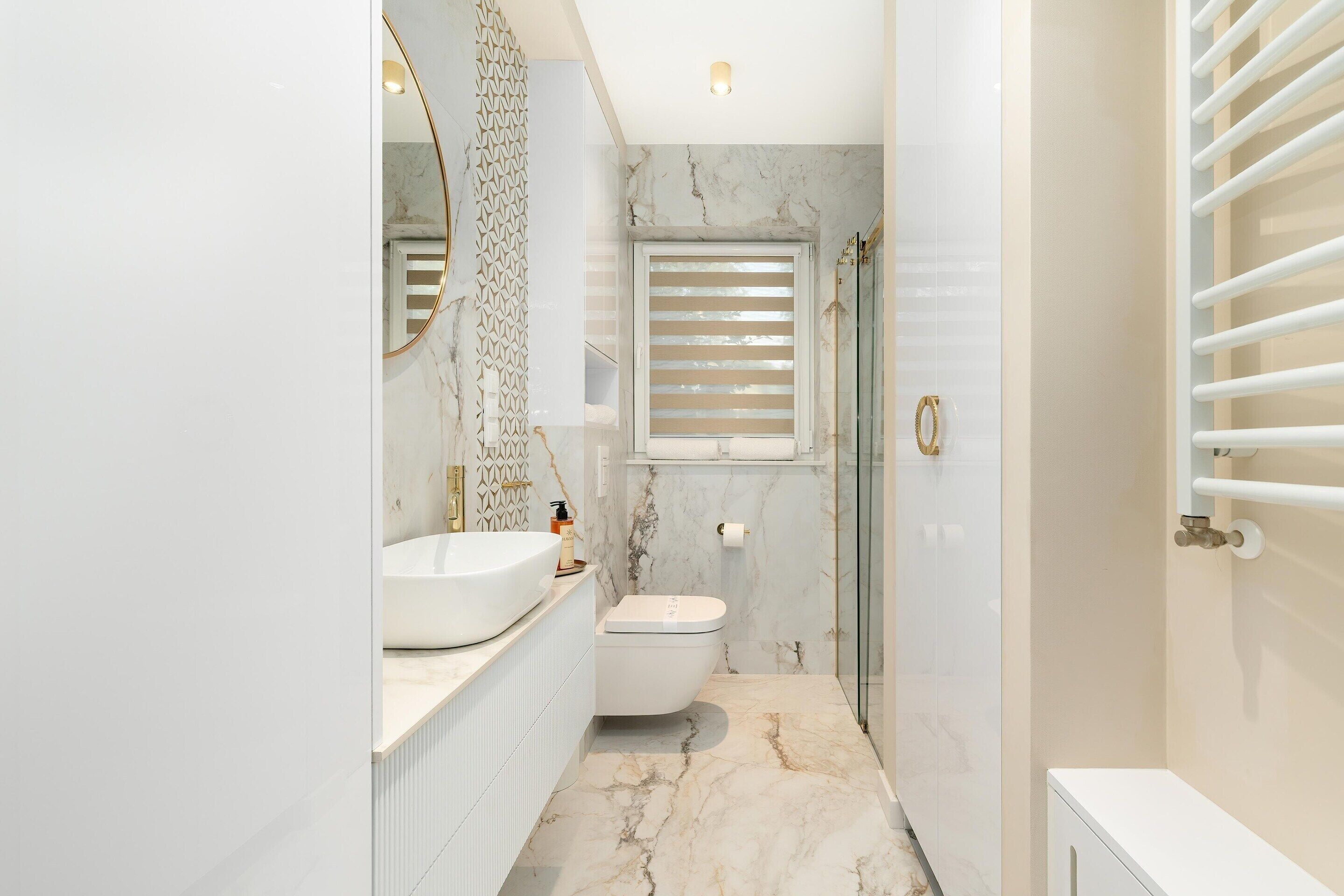 A modern bathroom with a marble floor, a white sink, a toilet, and a glass shower enclosure.