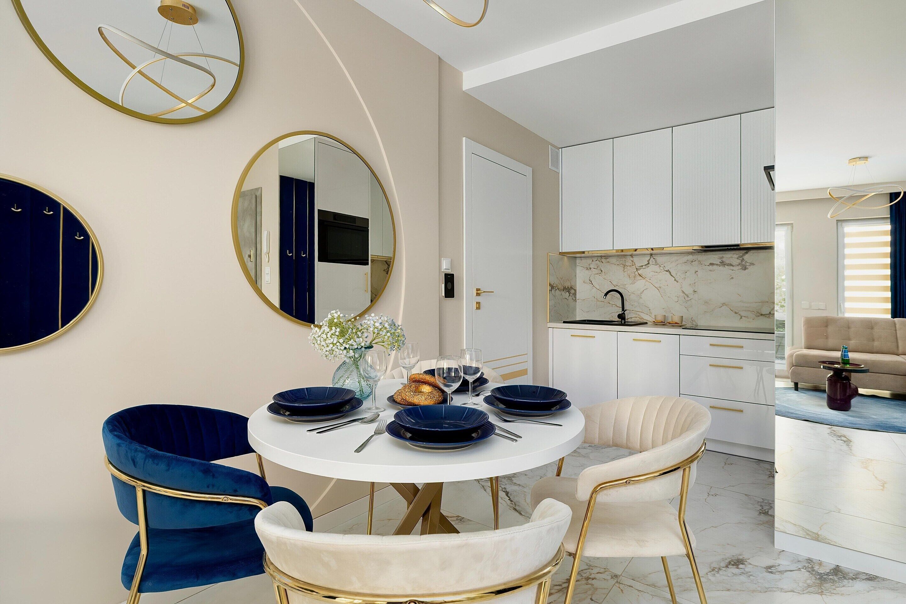 A modern dining area with a round table, blue and white chairs, and a kitchen in the background.