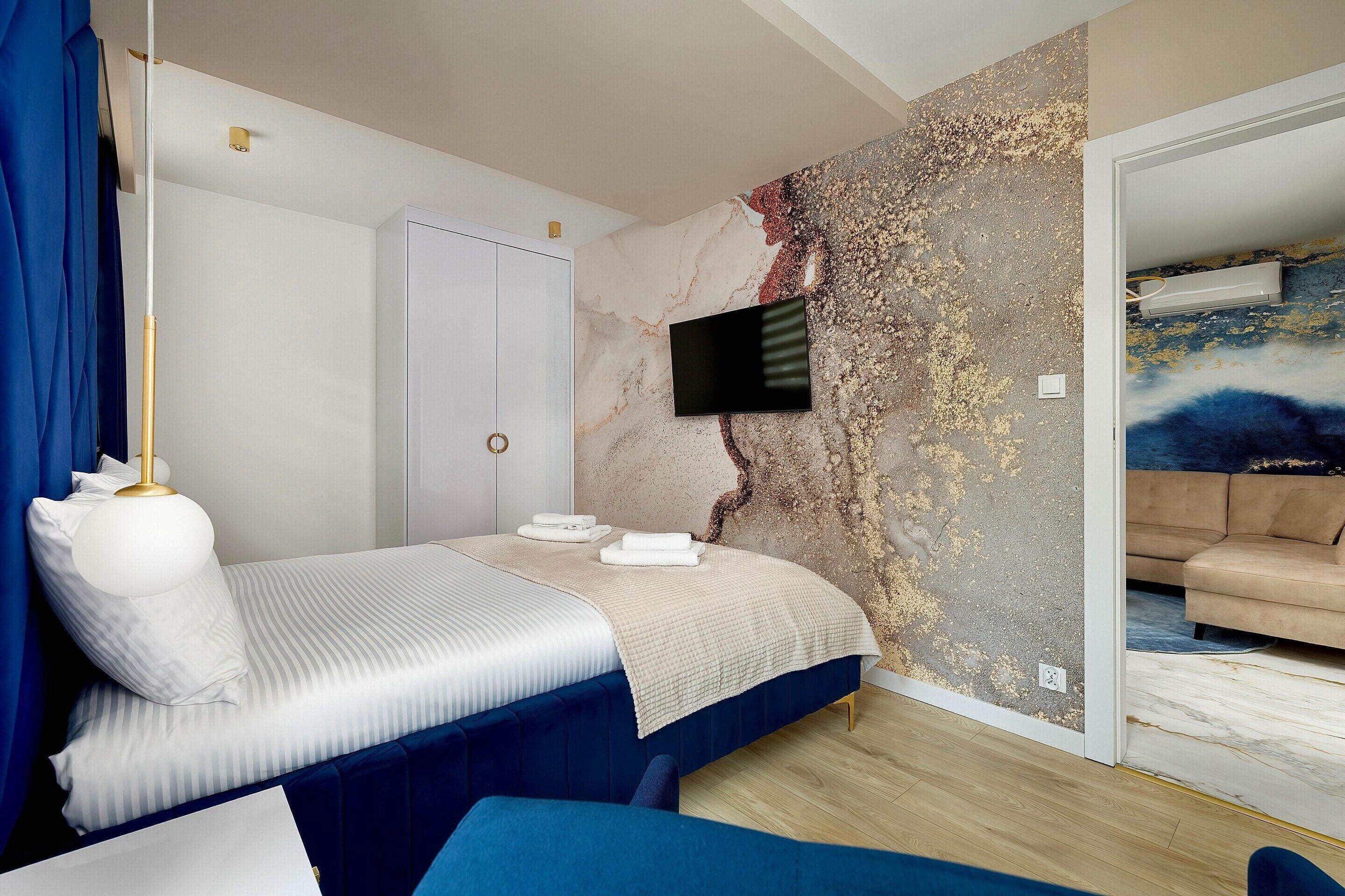 Une chambre à coucher comprenant un lit, un téléviseur fixé au mur, une armoire et un tableau accroché au mur adjacent.