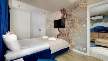 Un dormitorio con una cama, un televisor montado en la pared, un armario y un cuadro en la pared contigua.