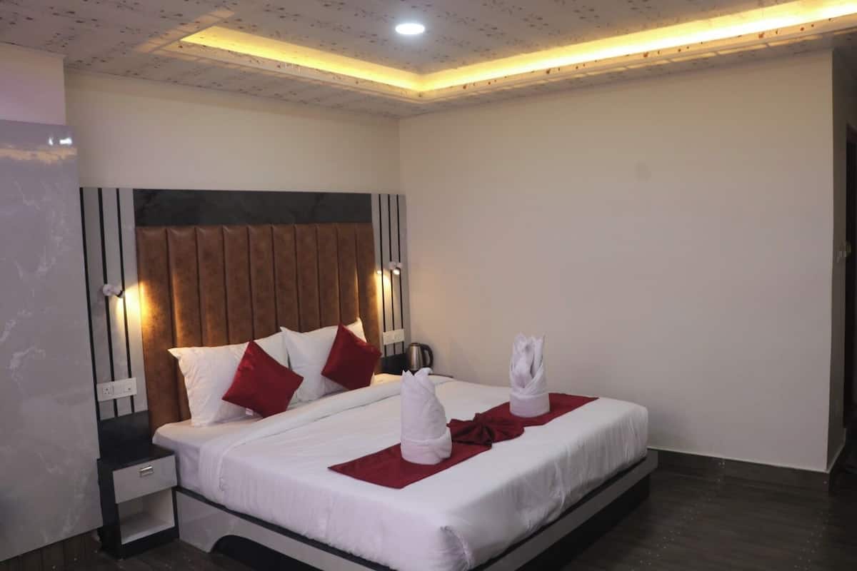 Una habitación de hotel con cama, mesita de noche, luz adosada a la pared y una toalla sobre la cama.