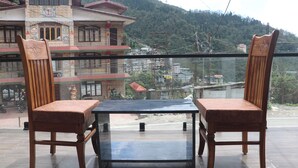 Un balcon avec deux chaises en bois et une table, donnant sur une région montagneuse parsemée de bâtiments.