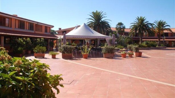 A courtyard with a white tent, potted plants, and a building with a red roof. - Residence Porto Coda Cavallo auf Sardinien (San Teodoro)