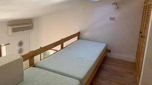 A small, single-room accommodation with a bunk bed, a skylight, a wooden door, and a wall-mounted air conditioning unit. - Residence Porto Coda Cavallo auf Sardinien (San Teodoro)