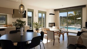 Et moderne interiør med spiseplads, sofa, TV og udsigt til en swimmingpool.