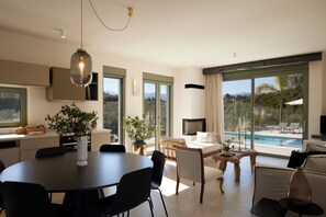 Ein modernes Interieur mit Essbereich, einer Couch, einem Fernseher und Blick auf einen Swimmingpool.
