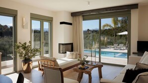 Et moderne hotelværelse med en stor skydedør, en sofa, et spisebord, et fjernsyn og udsigt til en swimmingpool.