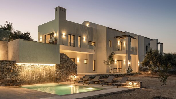Ein modernes, zweigeschossiges Haus mit Pool, Außenbereich und einem Wasserfall-Element aus Stein.