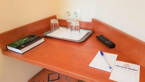 A small, orange desk with a book, a notepad, a pen, a tray with glasses, and a remote control. - Heléna Hotel & SPA (Levél)