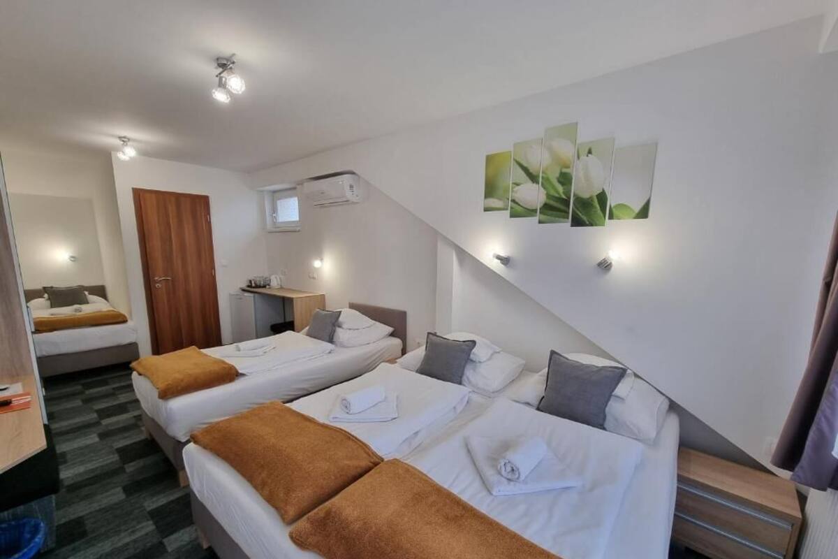 Habitación de hotel con dos camas, un armario de madera, un escritorio y aire acondicionado instalado en la pared.