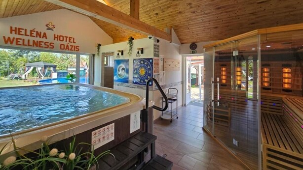 A wellness area with a hot tub, wooden ceiling, and a sign for Heléna Hotel Wellness Oázis. - Heléna Hotel & SPA (Levél)