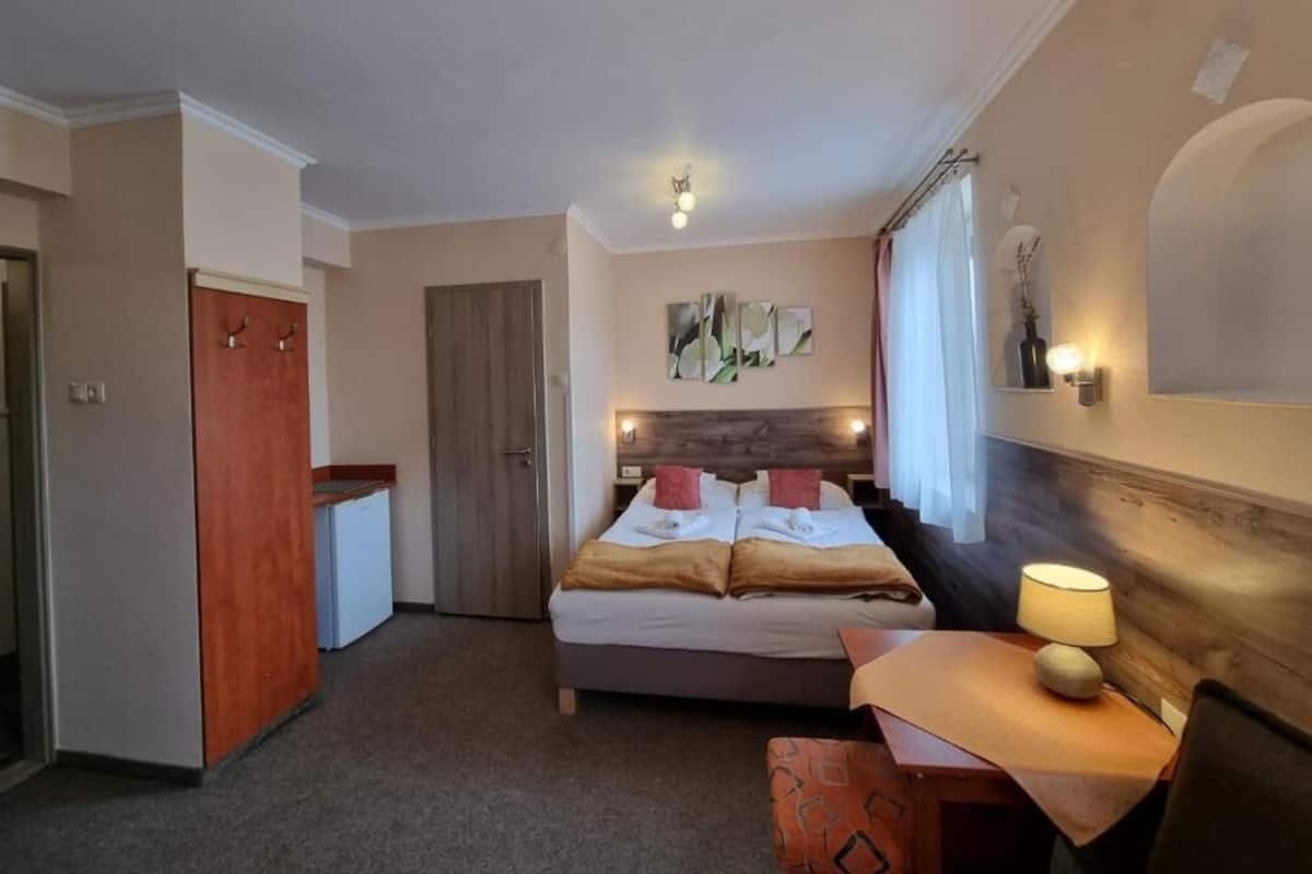 Una habitación de hotel con cama, mesita de noche, lámpara, una obra de arte y una puerta.