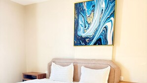 Un llit ben arrenjat amb roba blanca, un quadre abstracte blau a sobre i una catifes blava a ratlles al davant.