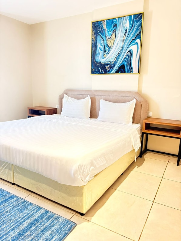 A neatly made bed with white linens, a blue abstract painting above it, and a blue striped rug in front.