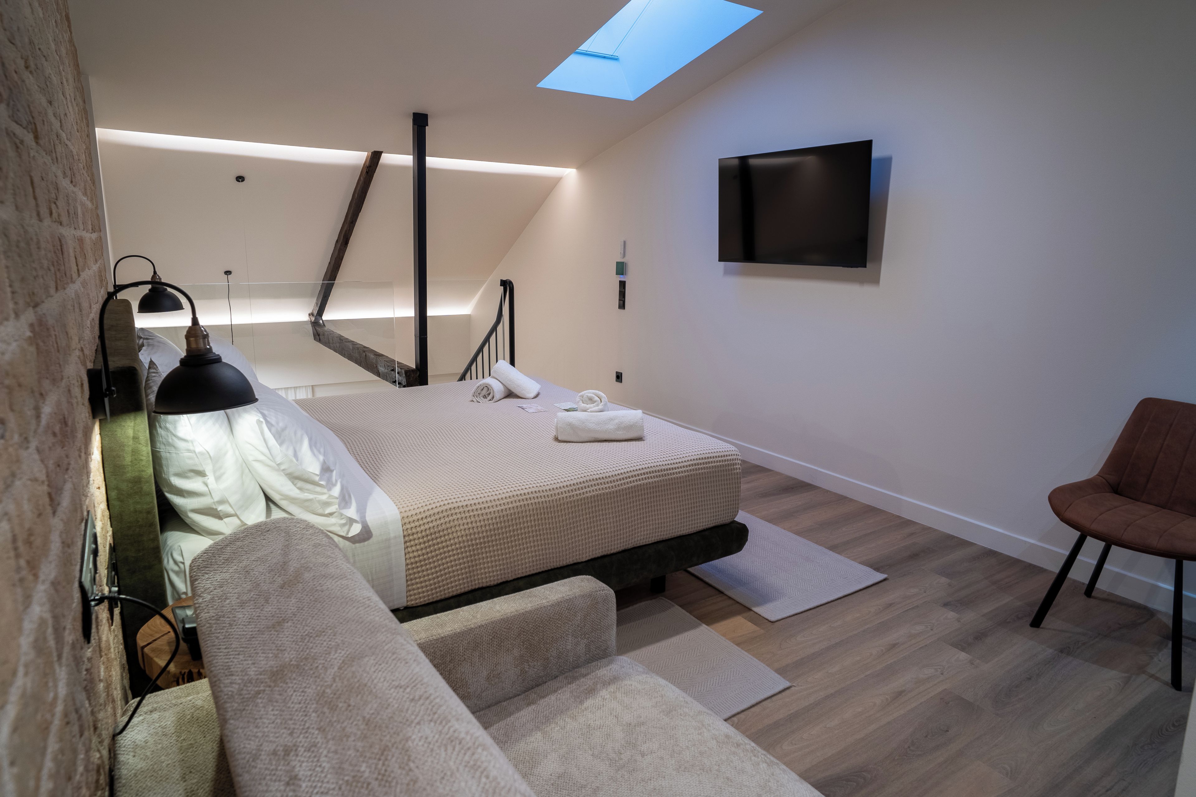 Un dormitorio moderno con cama, televisor, sofá y tragaluz.