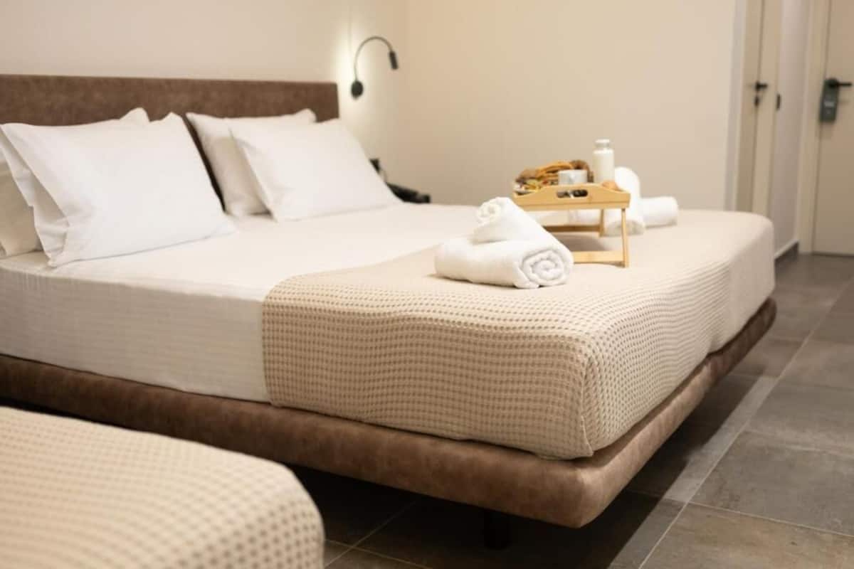 Un lit bien fait, avec une tête de lit marron, une table de chevet sur laquelle sont posés des articles de toilette et une lampe fixée au mur.