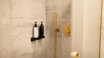 Un baño con ducha de oro, dispensador de jabón negro y una botella blanca sobre un estante negro.