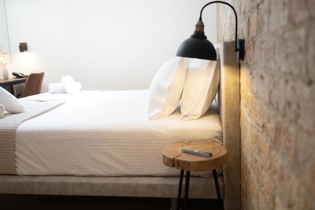 Una cama bien hecha con almohadas, una mesita de noche con un control remoto y una lámpara de pared.