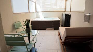 A compact room with a glass table, two chairs, a sofa, a storage unit, and a television.