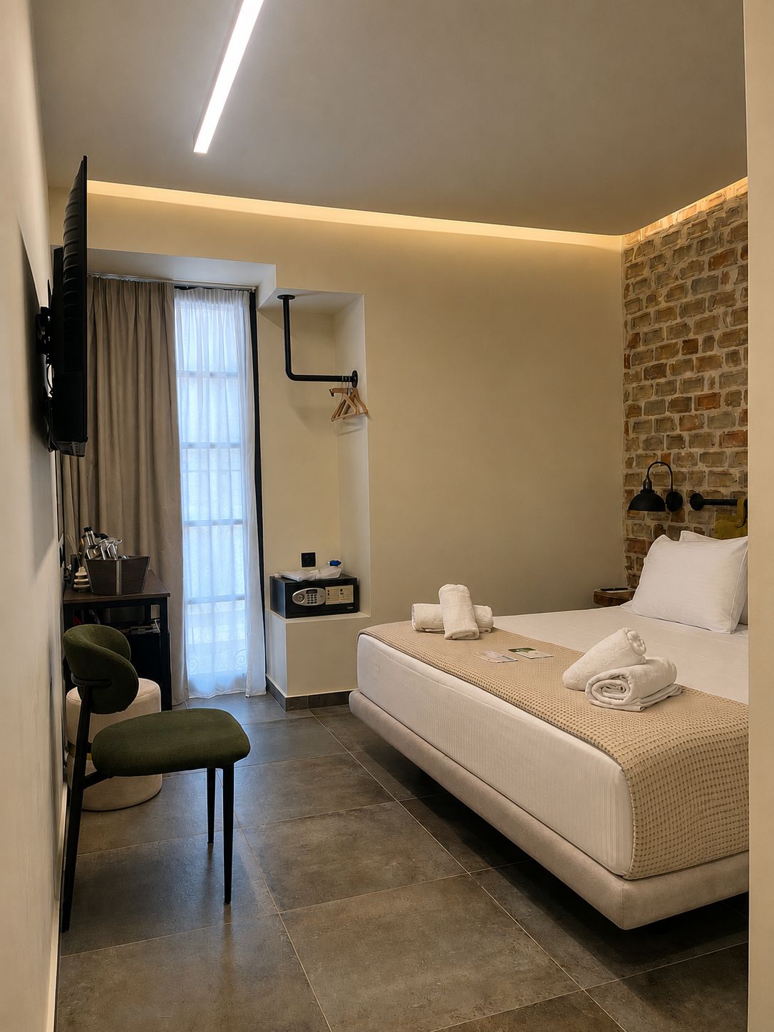 A modern hotel room with a bed, a desk, a chair, a television, and a brick wall.