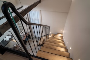 A wooden staircase with a glass railing, leading to a room with a table, a kettle, and a coffee machine.