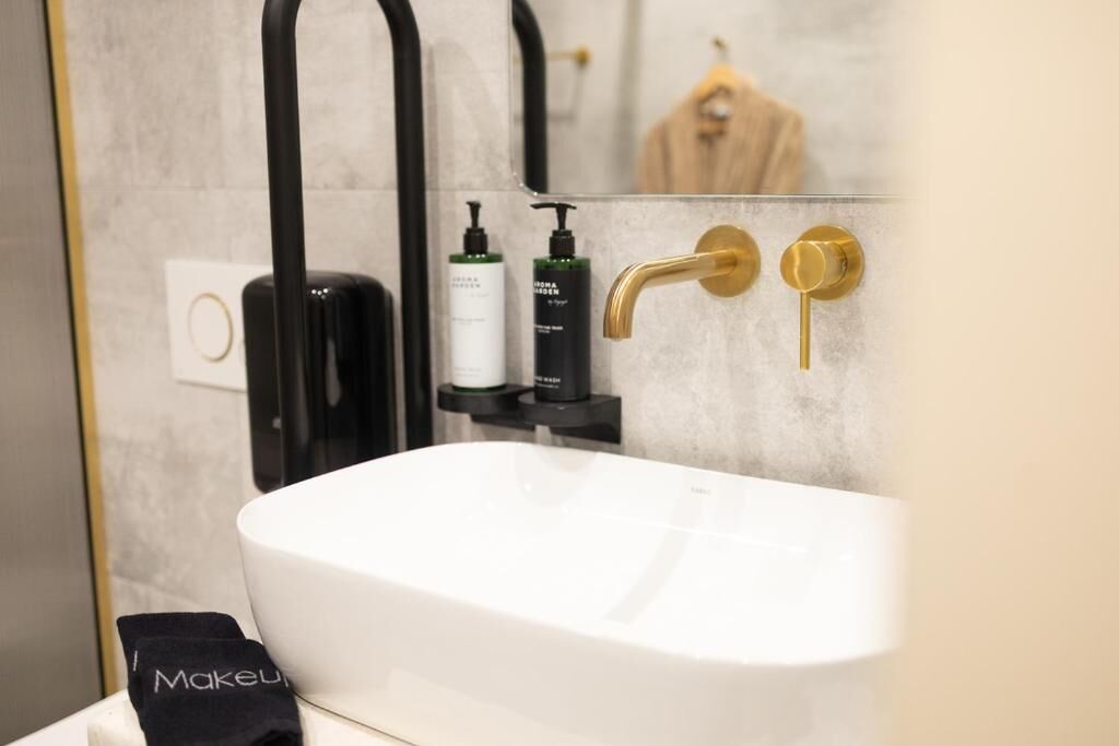 A bathroom with a white sink, black and gold fixtures, and a mirror reflecting a robe and a towel.