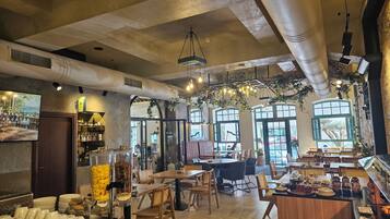 Caféinteriør med borde, stole, en kaffebar og store vinduer.