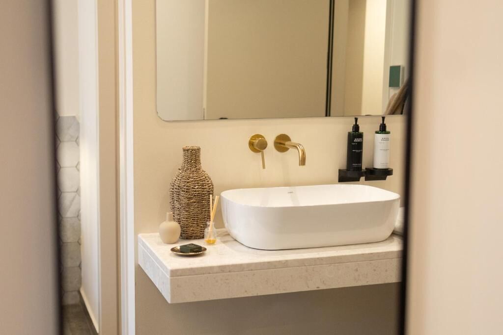 A bathroom with a white sink, gold faucet, and a mirror above.