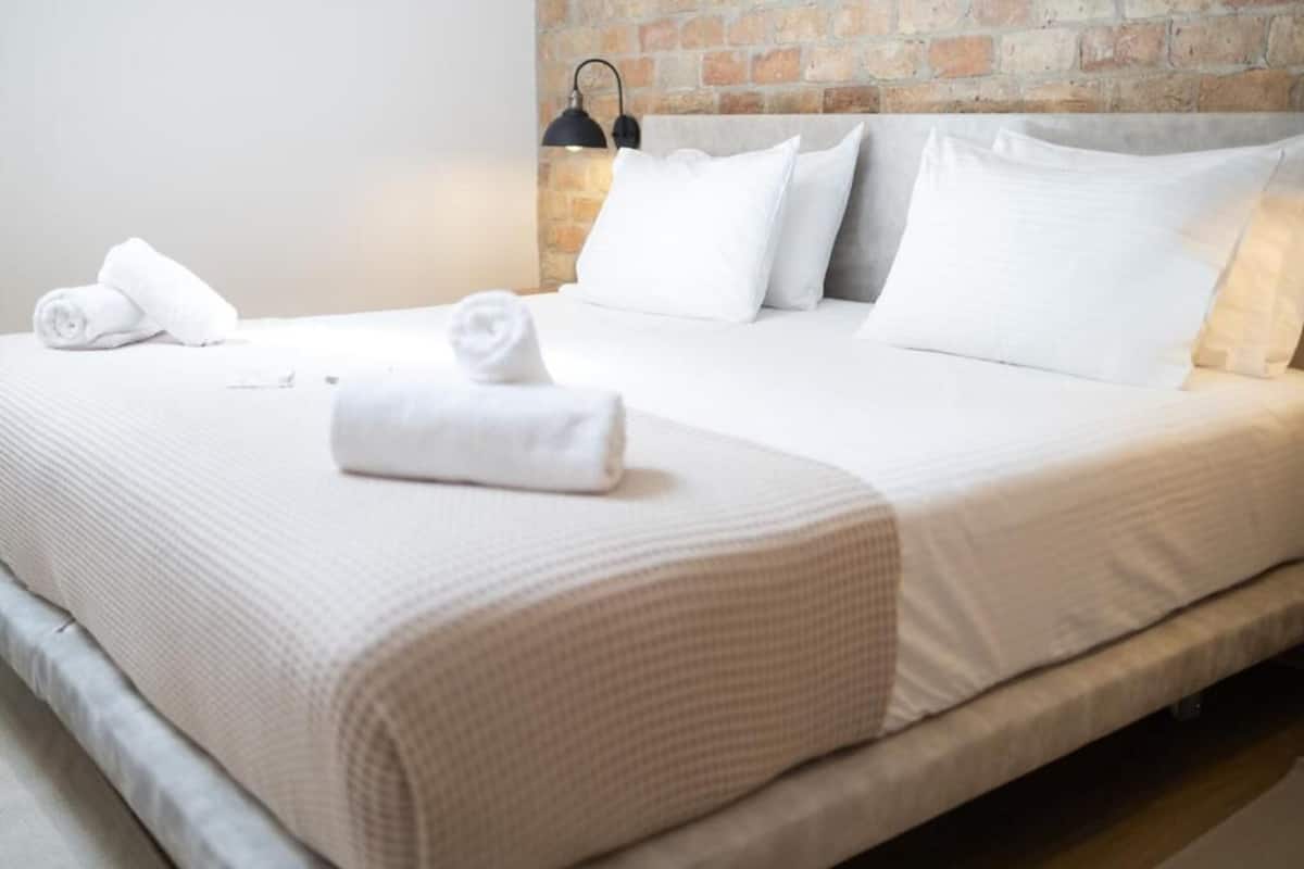 Un lit bien fait, avec du linge de lit blanc, un mur en briques et une seule lampe de chevet.