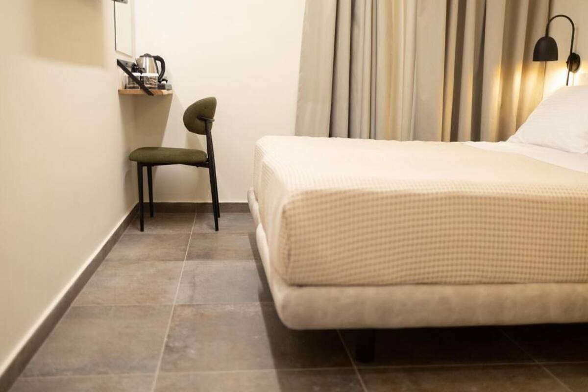 Une chambre d’hôtel avec un lit, une chaise, un bureau avec une lampe et une fenêtre avec des rideaux.