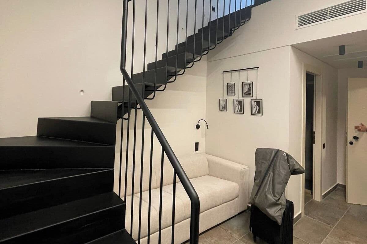 Un intérieur moderne avec un escalier noir, un canapé blanc et un fauteuil recouvert de tissu.