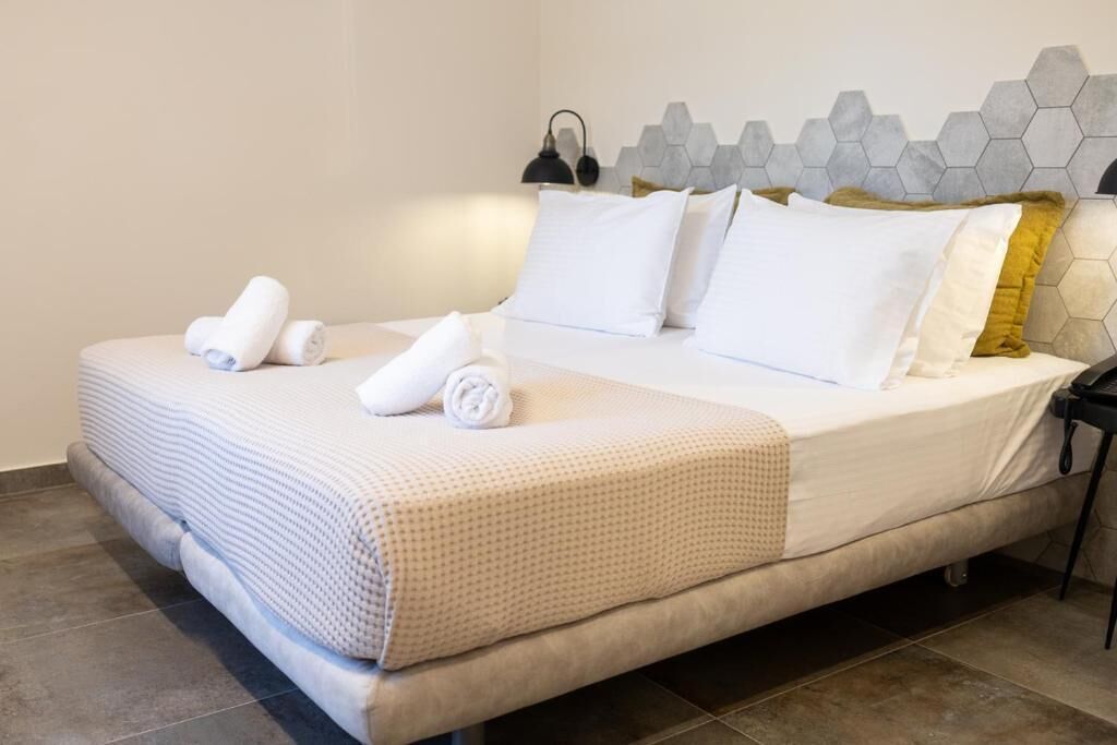 A neatly made bed with white linens and a patterned blanket, a headboard with a geometric design, and a bedside table with a lamp.