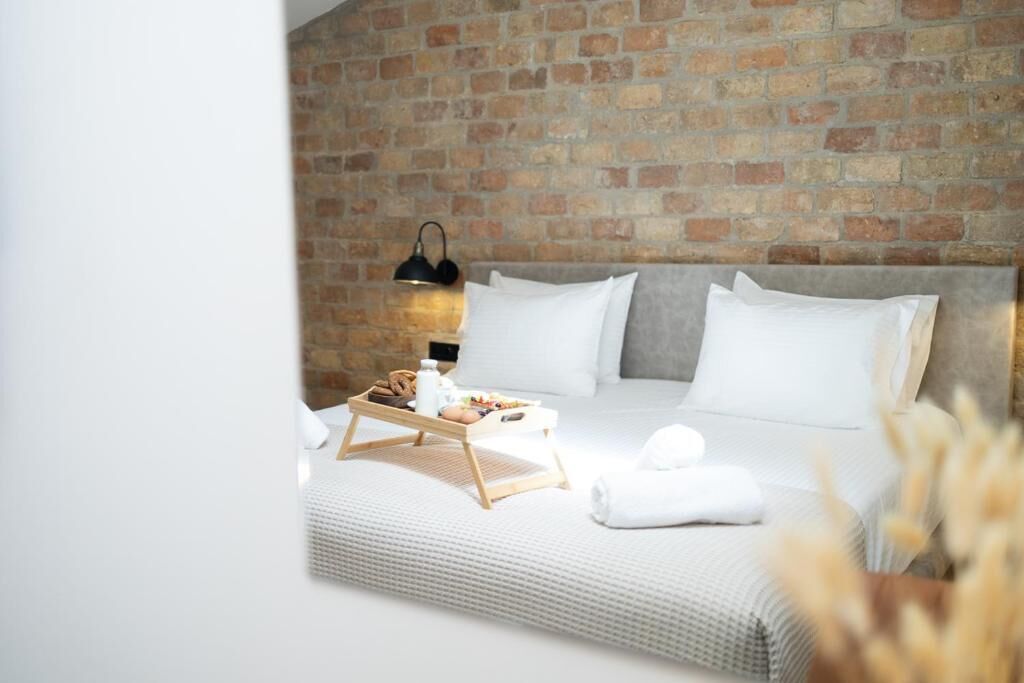 Een hotelkamer met een bakstenen muur, een bed met wit beddengoed, een nachtkastje met een ontbijtplateau en een lamp.