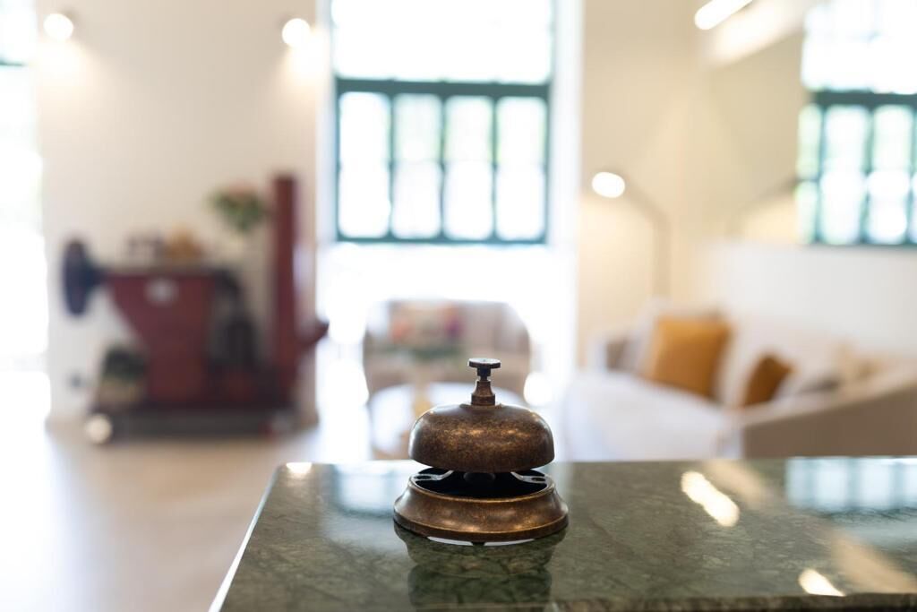 A brass bell on a marble table in a well-lit room with a sofa and a window in the background.