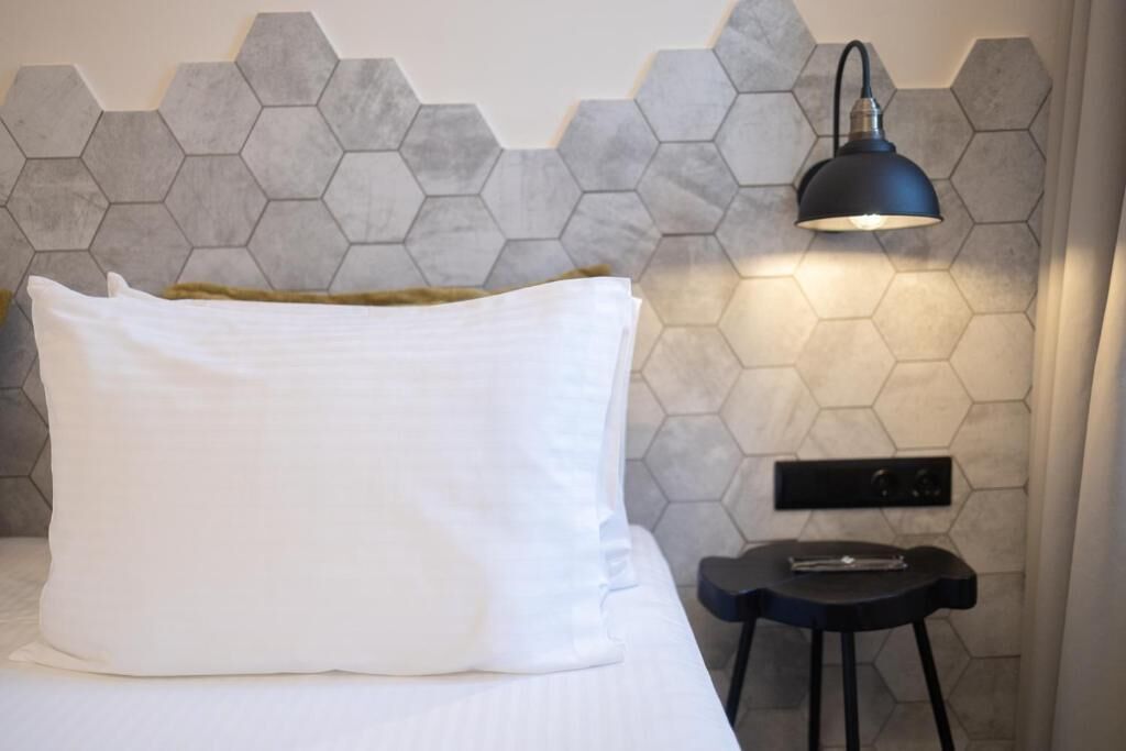 Una cama con un almohadón blanco, una lámpara negra y un diseño de pared hexagonal.